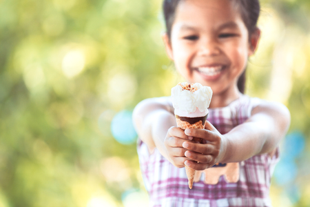 Cute asian little child girl holding delicious icecream cone in hand with fun and happinessの写真素材