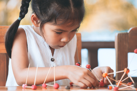 Cute asian child girl playing and creating with play dough and toothpick. Child concentrated with play dough building a molecule model.の写真素材