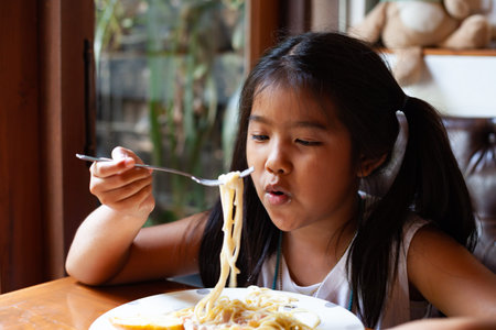 Asian child girl eating delicious Spaghetti Carbonara in the restaurantの写真素材