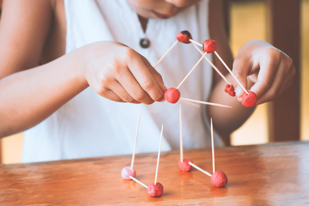 Cute asian child girl playing and creating with play dough and toothpick. Child concentrated with play dough building a molecule model.の写真素材