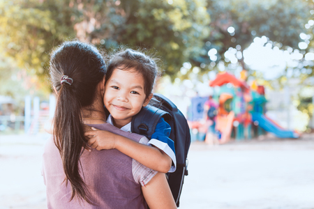 Back to school. Cute asian pupil girl with backpack hugging her mother in the playground before go to classroom in the school.の写真素材