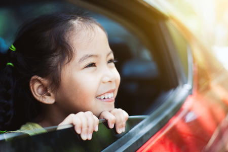 Cute asian little child girl smiling and having fun to  travel by car and looking out from car window in the countrysideの写真素材