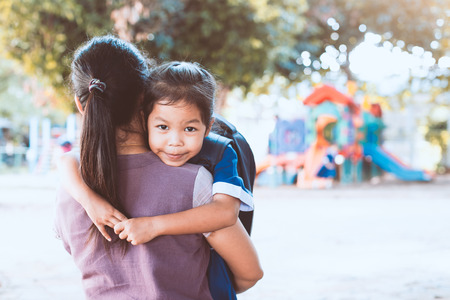 Back to school. Cute asian pupil girl with backpack hugging her mother in the playground before go to classroom in the school.の写真素材