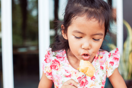 Cute asian little child girl eating delicious toast for breakfast with happinessの写真素材
