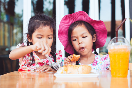 Two cute asian little child girls eating delicious toast and orange juice for breakfast together with happinessの写真素材