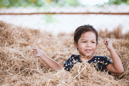 Cute asian child girl having fun to play with hay stack in the farm with happinessの写真素材