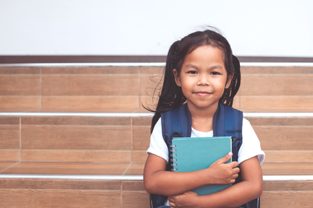 Back to school. Cute asian child girl with school bag holding a book at schoolの写真素材