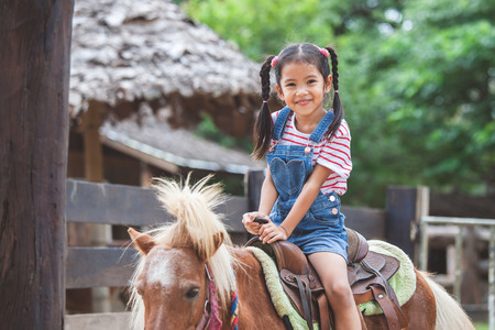 Cute asian child girl riding a pony in the farm with funの写真素材