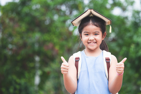 Back to school. Cute asian child girl with school bag put a book on head and love to go to schoolの写真素材