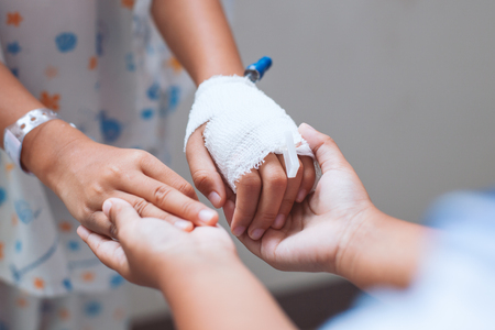 Child girl holding sick young sister hand who have IV solution bandaged with love and care in the hospitalの写真素材