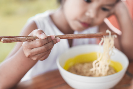 Closeup on hand of child girl holding chopstick while she is eating instant noodles in white bowlの写真素材
