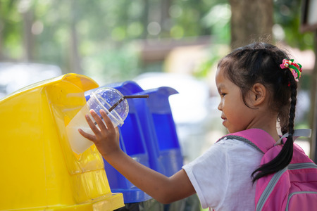 Cute Asian child girl throwing plastic glass in recycling trash bin at public parkの写真素材