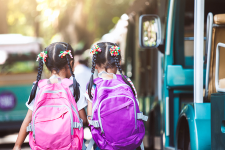 Asian pupil kids with backpack holding hand and going to school with school bus together. Back to school concept.の写真素材