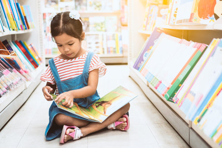Cute asian child girl select book and reading a book in bookstore in supermarketの写真素材
