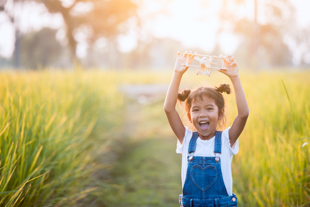 Cute asian child girl playing with toy wooden airplane in the field at sunset time with funの写真素材