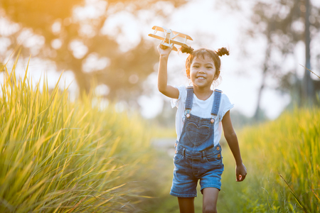 Cute asian child girl running and playing with toy wooden airplane in the field at sunset time with funの写真素材