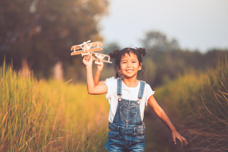 Two cute asian child girls running and playing with toy wooden airplane in the field at sunset time together with funの写真素材