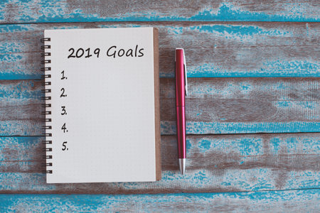 2019 goals list with notebook and pen on rustic blue wooden table