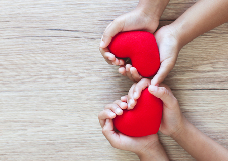 Red heart in child hands on wooden table background with love and harmonyの写真素材
