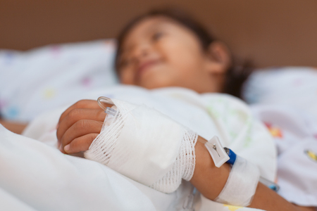 Sick asian little child girl hand who have saline intravenous (iv) drip bandage is sleeping on bed in the hospitalの写真素材