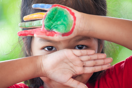 Cute asian little child girl with painted hands closed her face and showing only her eyesの写真素材