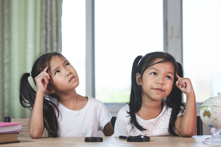 Two cute asian child girls thinking when doing homework in the room togetherの写真素材