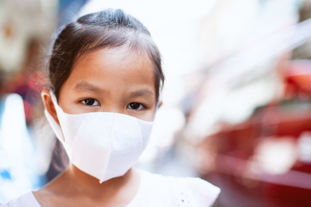 Cute asian child girl wearing protection mask to against air smog pollution with PM 2.5 in the cityの写真素材