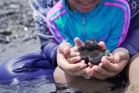 Mother and her daughter holding beautiful pebble stones in hands together in the seaの写真素材