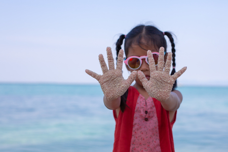 Asian child hands with sand having fun on the beachの写真素材