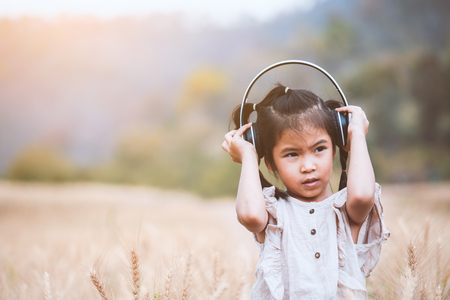 Cute asian child girl having fun to listen the music with headphones in the barley field with happinessの写真素材