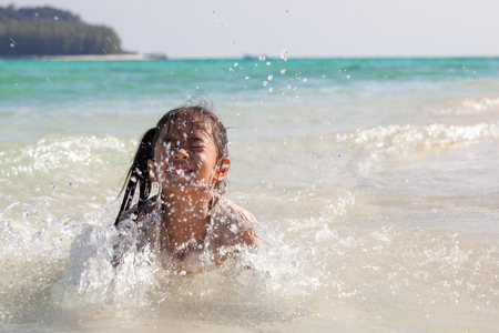 Happy asian child girl having fun to play water in the beautiful sea in summer vacationの写真素材