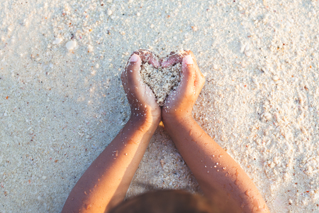 Child girl holding sand make heart shape in hands and playing on the beach in summer vacationの写真素材