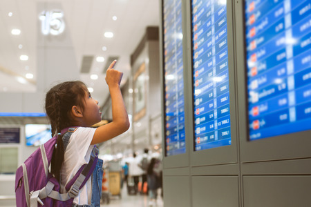 Cute asian child girl with backpack checking her flight at information board in international airport terminalの写真素材