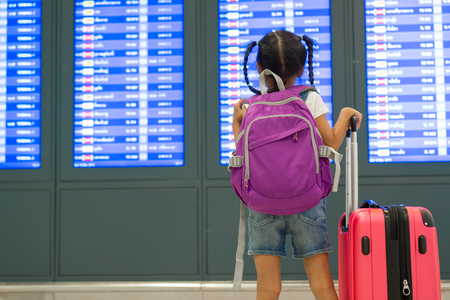 Cute asian child girl with backpack checking her flight at information board in international airport terminalの写真素材