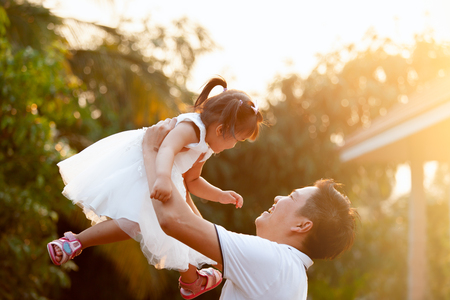 Asian father carrying his daughter up in the air and playing together in the park with fun and loveの写真素材