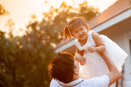 Asian father carrying his daughter up in the air and playing together in the park with fun and loveの写真素材