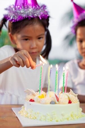 Cute asian child girl lighting candle on birthday cake in birthday partyの写真素材