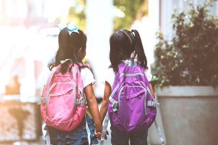 Back to school. Two cute asian child girls with school bag holding hand and walk together in the schoolの写真素材