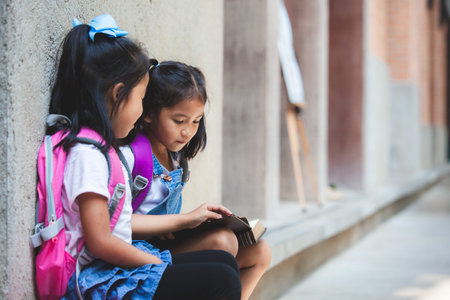 Back to school concept. Two cute asian pupil girls reading a book  together in the school with fun and happinessの写真素材