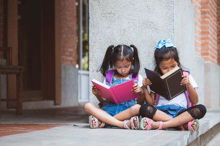 Back to school concept. Two cute asian pupil girls reading a book  together in the school with fun and happinessの写真素材