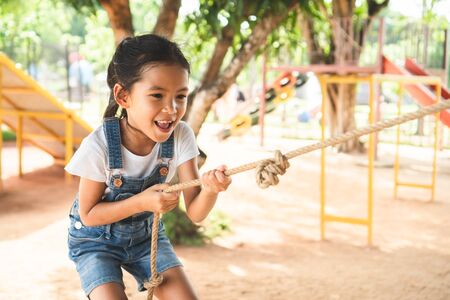 Cute asian child girl is climbing a wooden wall with a rope in the playground with fun and strongの写真素材
