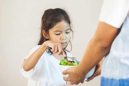 Mother give a bowl of salad to asian child girl to eat healthy vegetables for her mealの写真素材