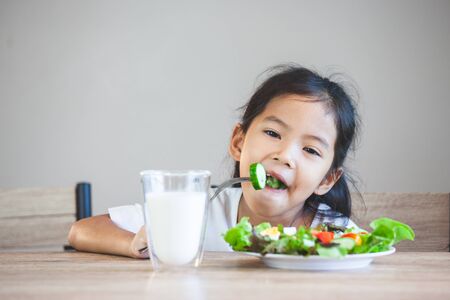 Cute asian child girl eating healthy vegetables and milk for her mealの写真素材