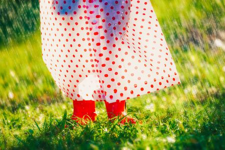 Asian girl with raincoat and red boots is walking under the rain in the meadowの写真素材