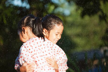 Two asian child girls wearing raincoat hugging each other with love in the rainy dayの写真素材