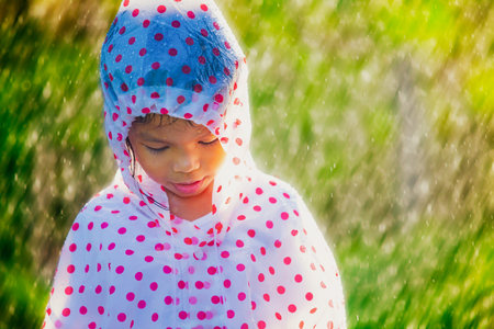 Sad asian child girl wearing raincoat standing under the rain in the rainy day