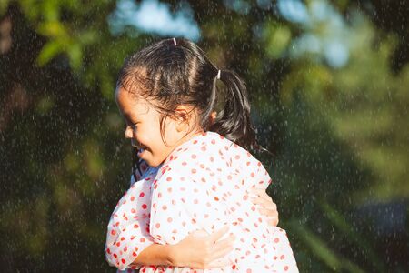Two asian child girls wearing raincoat hugging each other with love in the rainy dayの写真素材