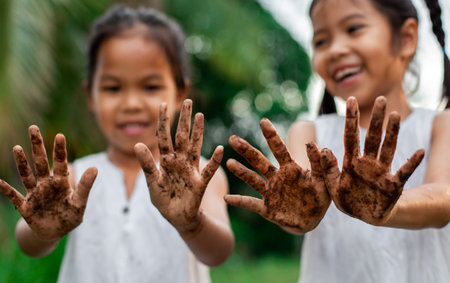 Two cute asian child girls showing dirty hands after planting the tree together in the garden