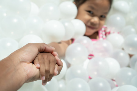 Parent holding daughter hand while she is playing with white plastic balls in the playgroundの写真素材