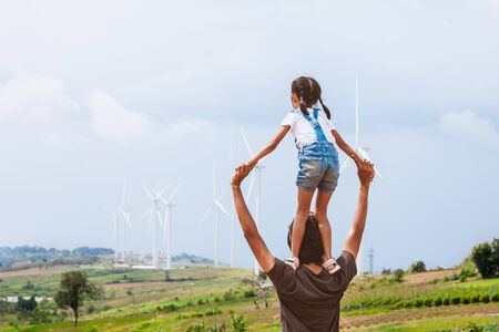 Father and daughter having fun to play together. Asian child girl riding on father's shoulders in the wind turbine fieldの写真素材